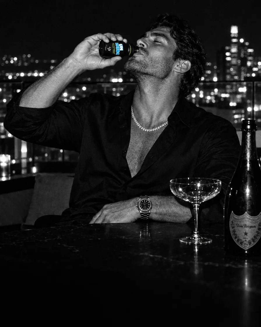 Man in a black shirt drinking an UNHUNG shot on a rooftop at night